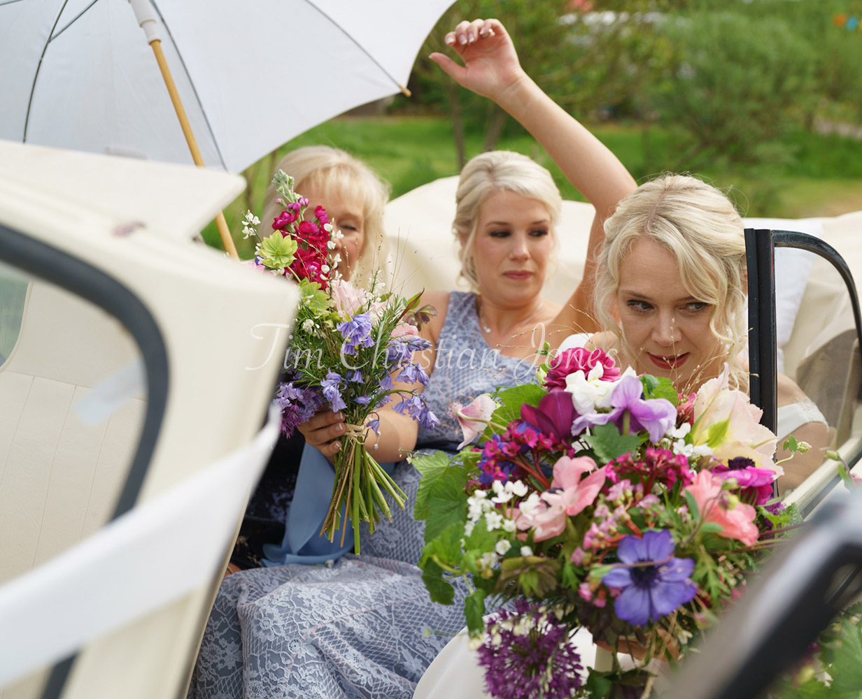 Bride arriving in a cream Morris Minor with umbrella raised, captured candidly.