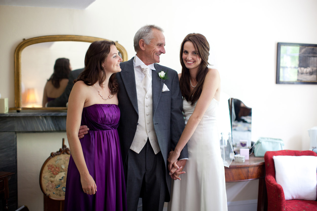 Bride standing with her father and sister, a relaxed family moment full of genuine connection.