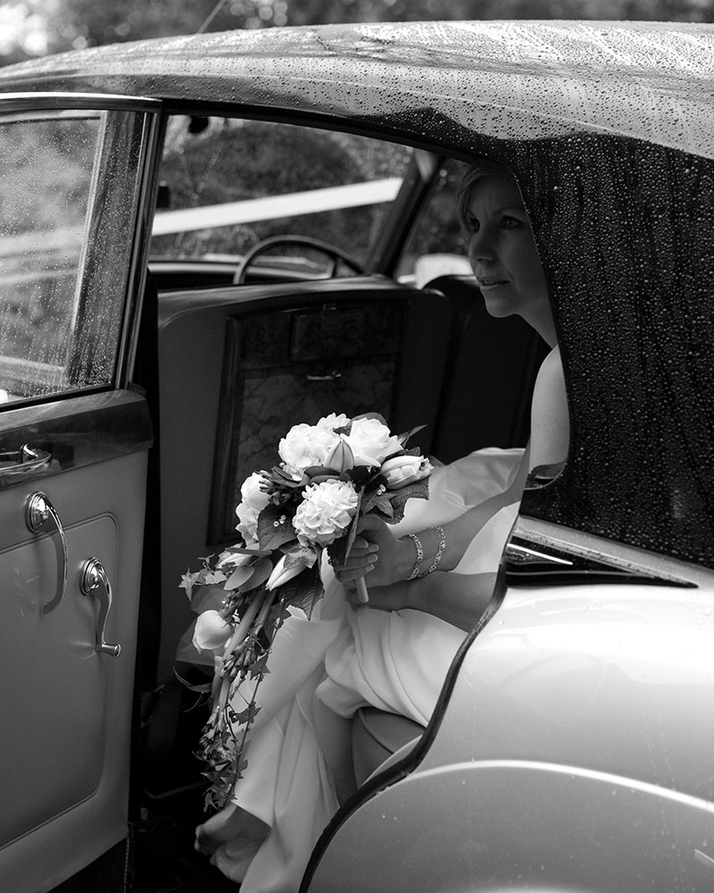 Candid moment as the bride waits in the vintage wedding car for the rain to settle.