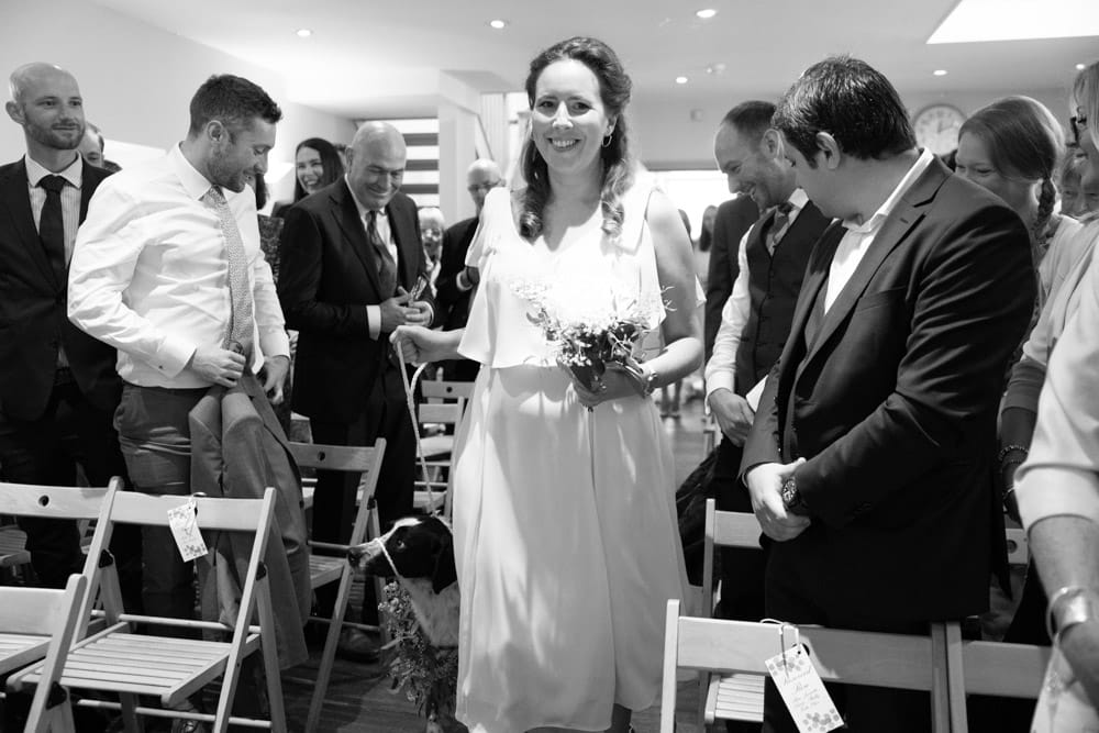 In black and white, the first bridesmaid smiles as she reaches the aisle’s end.