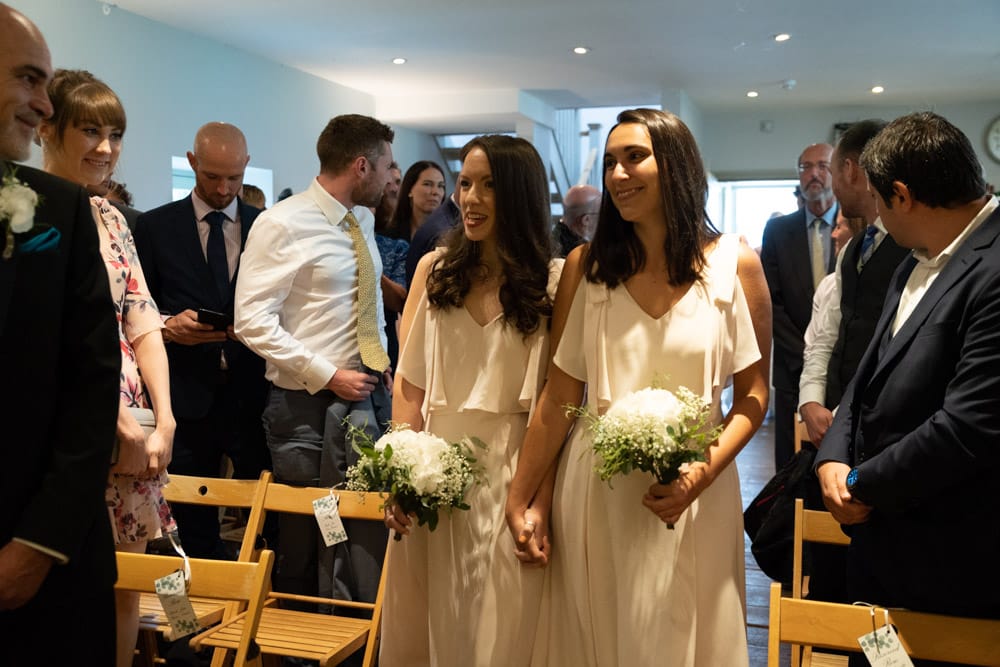 Two bridesmaids walk hand in hand, smiling at guests during wedding ceremony at The Chilli Barn in Otley.