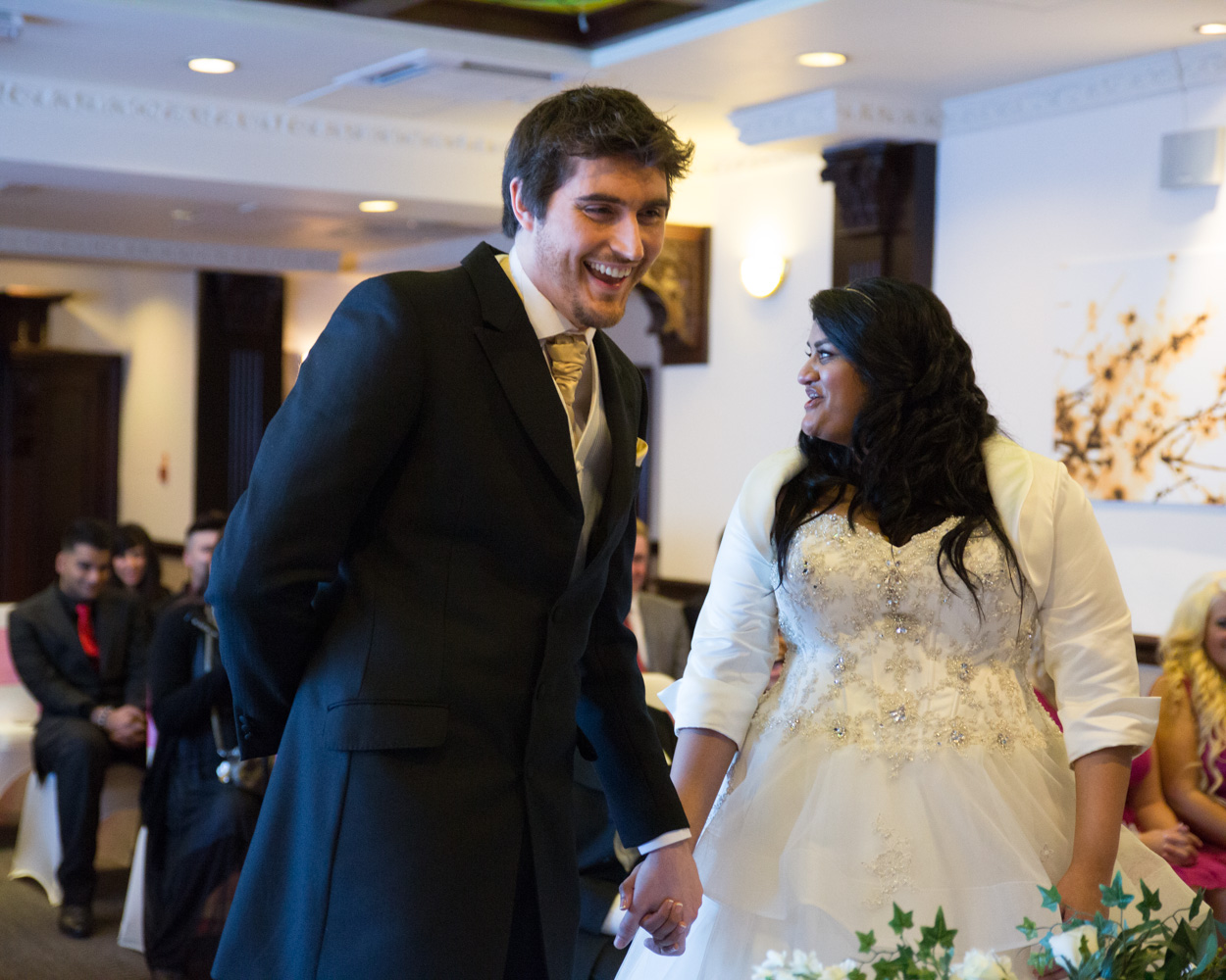 Groom looks up and smiles at guests while pretending to sign the register