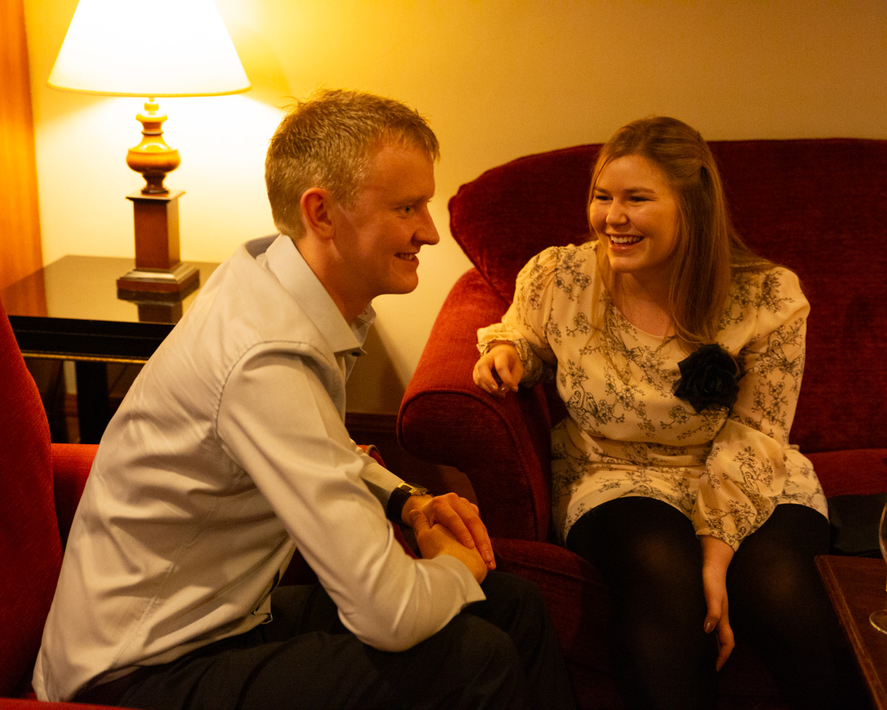 Guest couple seated, surrounded by friends and smiling naturally