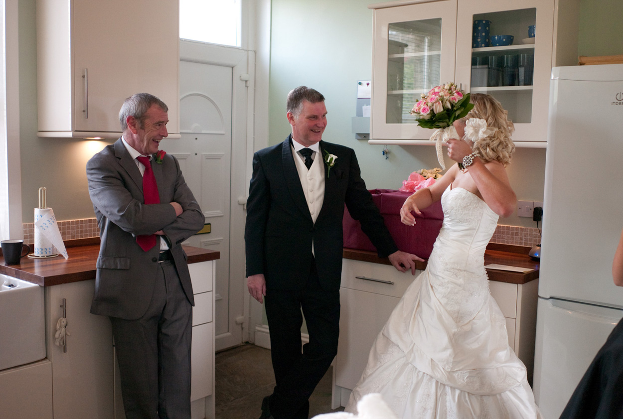 Dani playfully lifts her pink rose bouquet while walking with her dad and uncle