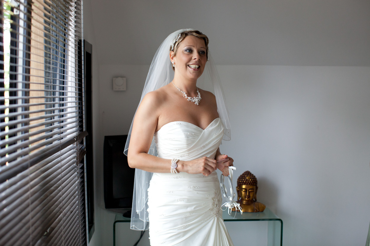 Bride in natural light near venetian blinds, calm and radiant.
