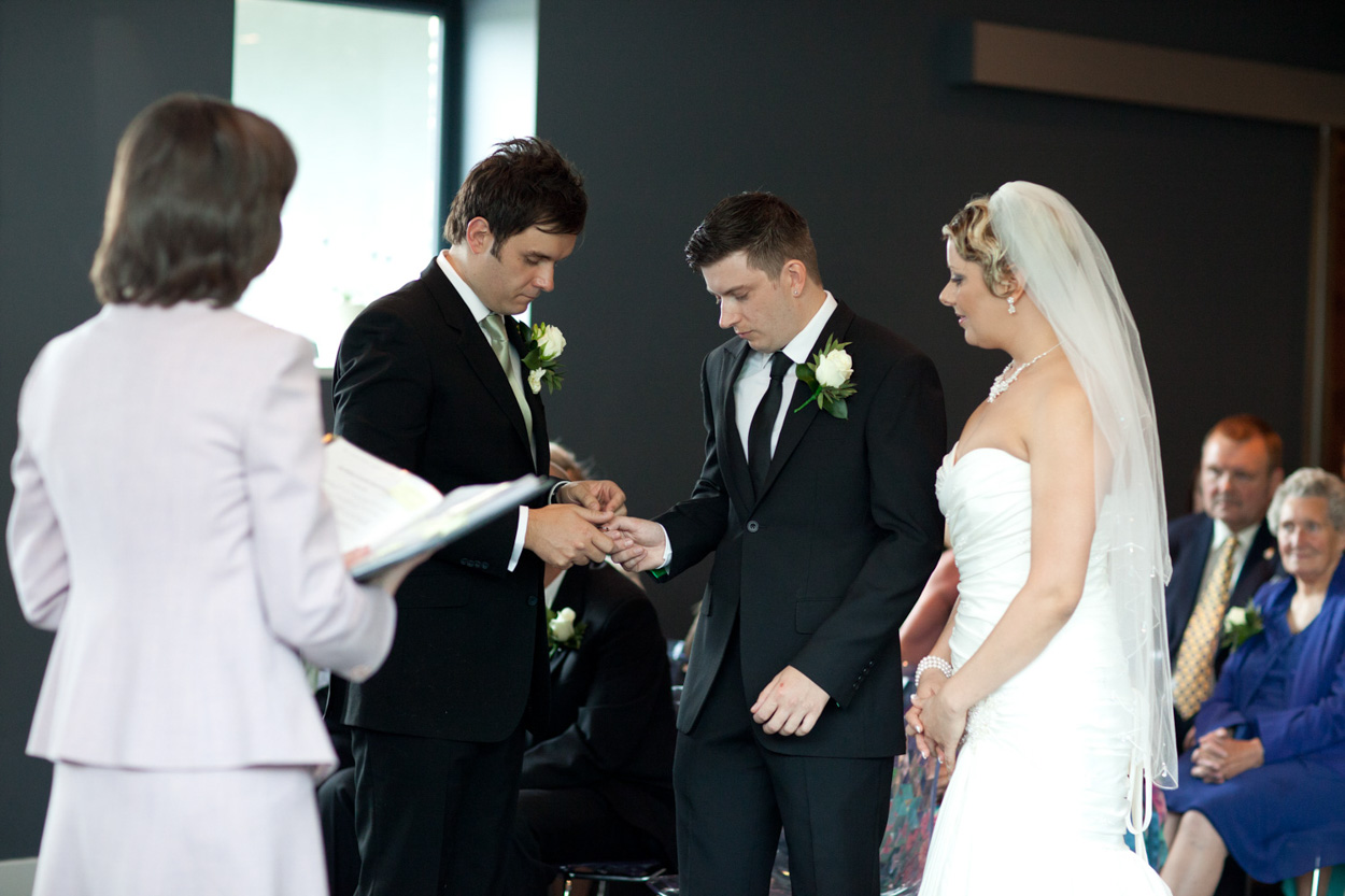 Best man passes the ring to Tim, while Sam watches intently.