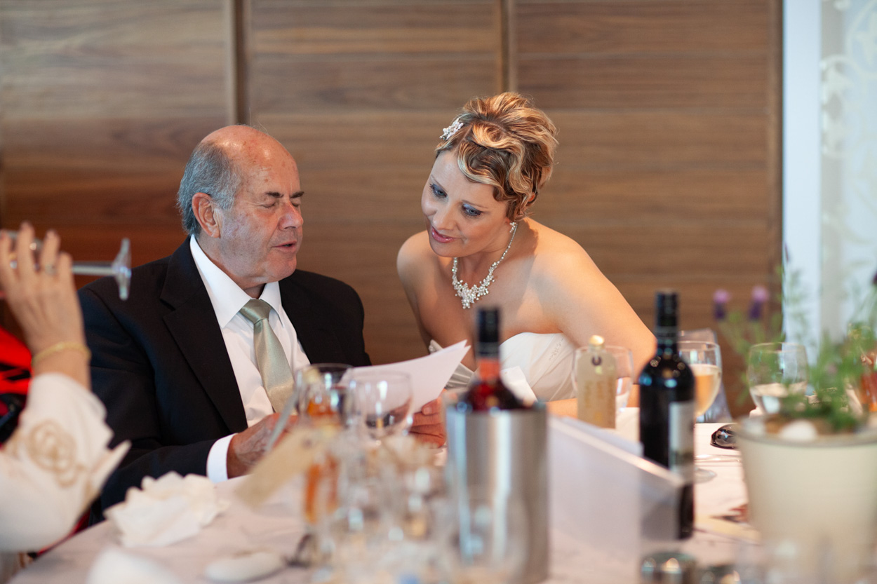 A man helps his little son at the table, the boy trying to cut bread with a pencil.