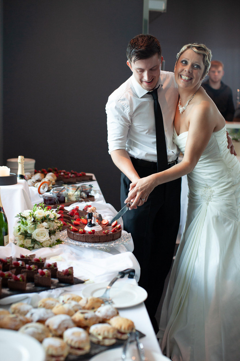 The couple smile as they look closely at their unique cake topper.