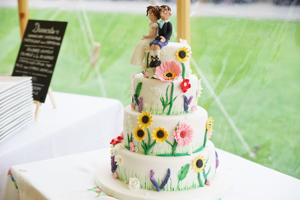 Colourful floral 4-tier wedding cake in the subtle light of a marquee wedding breakfast - photographed by Tim Christian Jones | Leeds wedding photographer