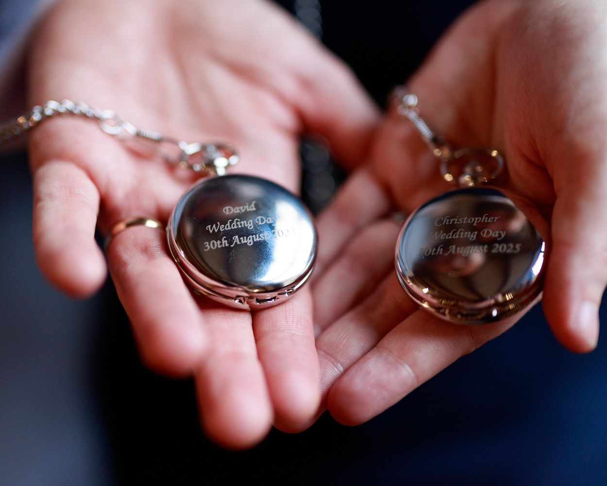 Grooms' pocket watches with engraved wedding date and names in the hands of the couple