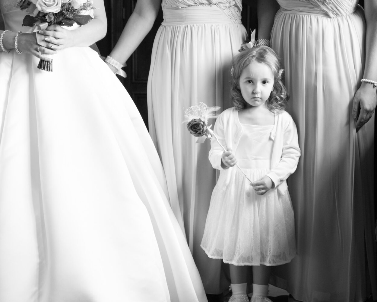 Cute little bridesmaid stands a bit lost in thought during a wedding ceremony in monochrome