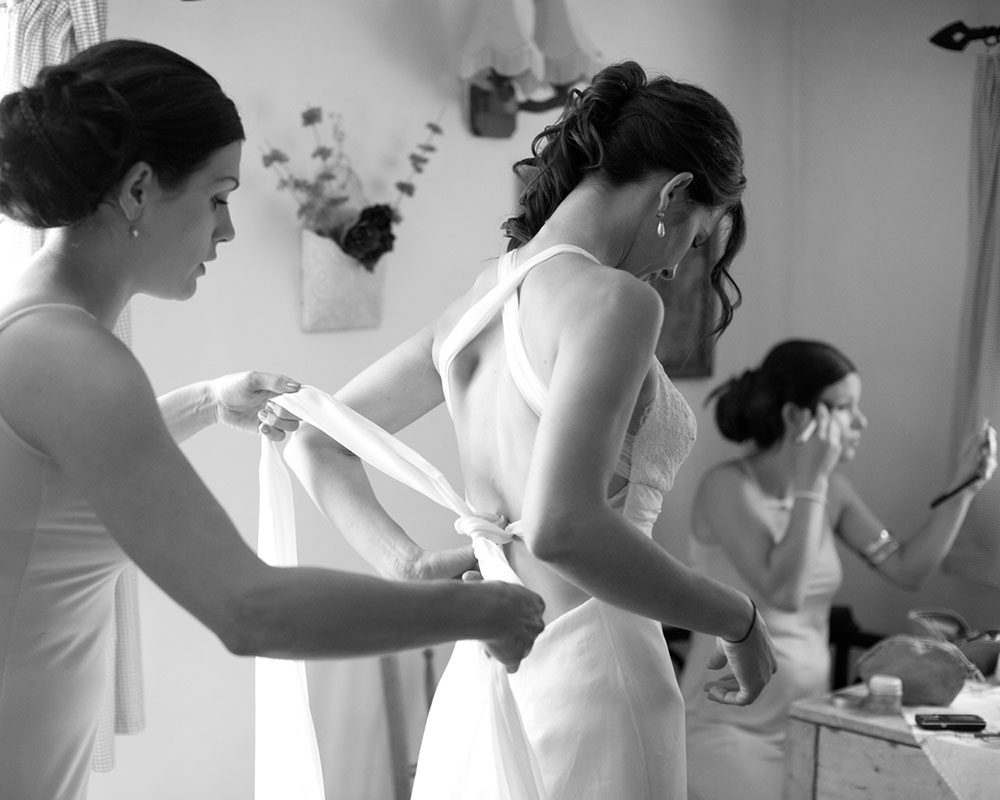 Bridal preparation as bridesmaids help with hair and dress in black and white.