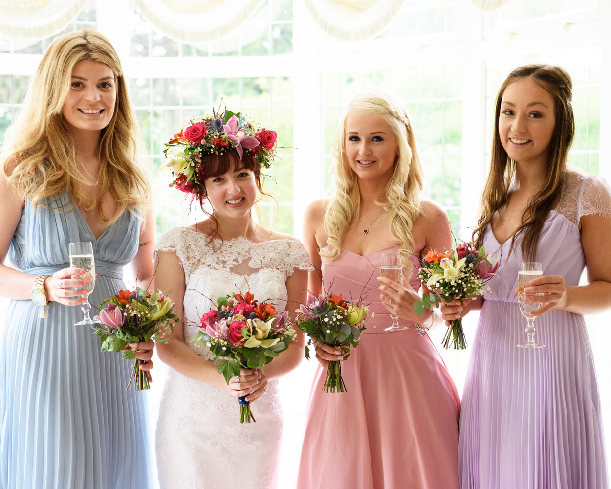 Bride and bridesmaids in pink and blue dresses with bouquets and champagne.