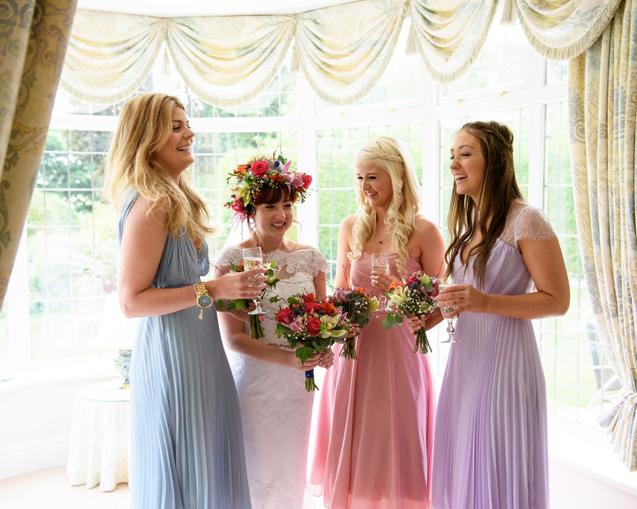 Bride and bridesmaids stand outside on a garden path surrounded by trees and light.