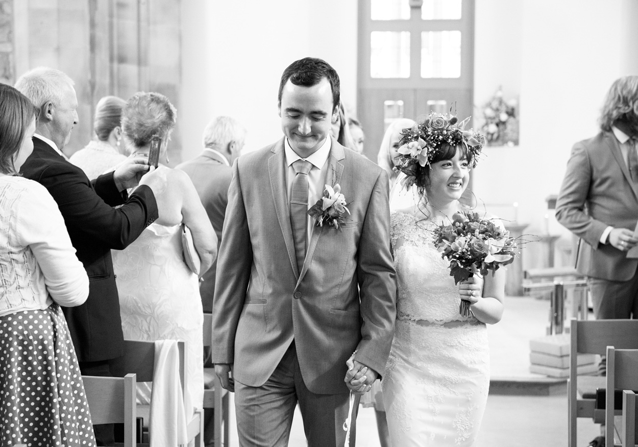Bride and groom look over a stone wall at the stream beside the church.