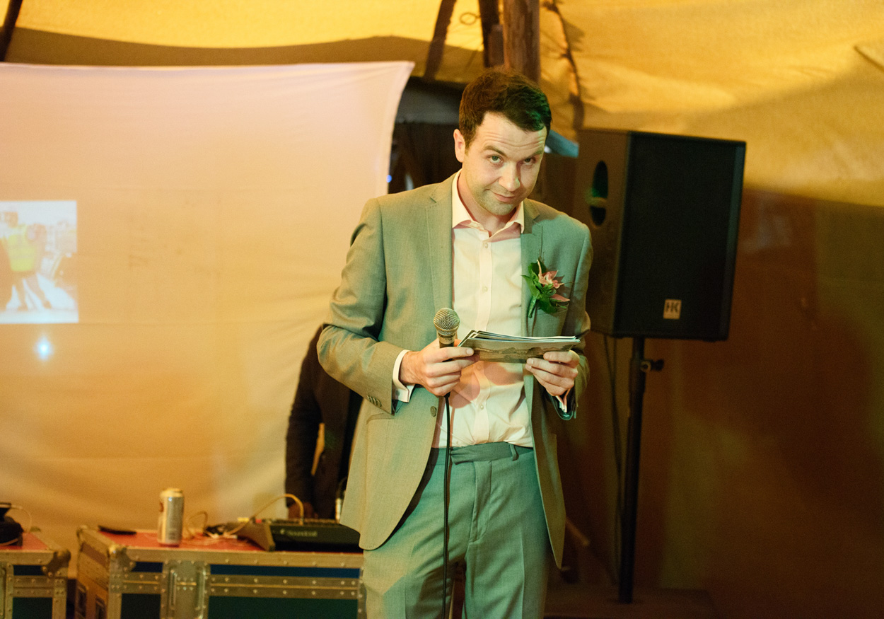 Guest in orange wig, yellow garland, and funny glasses poses at the wedding.