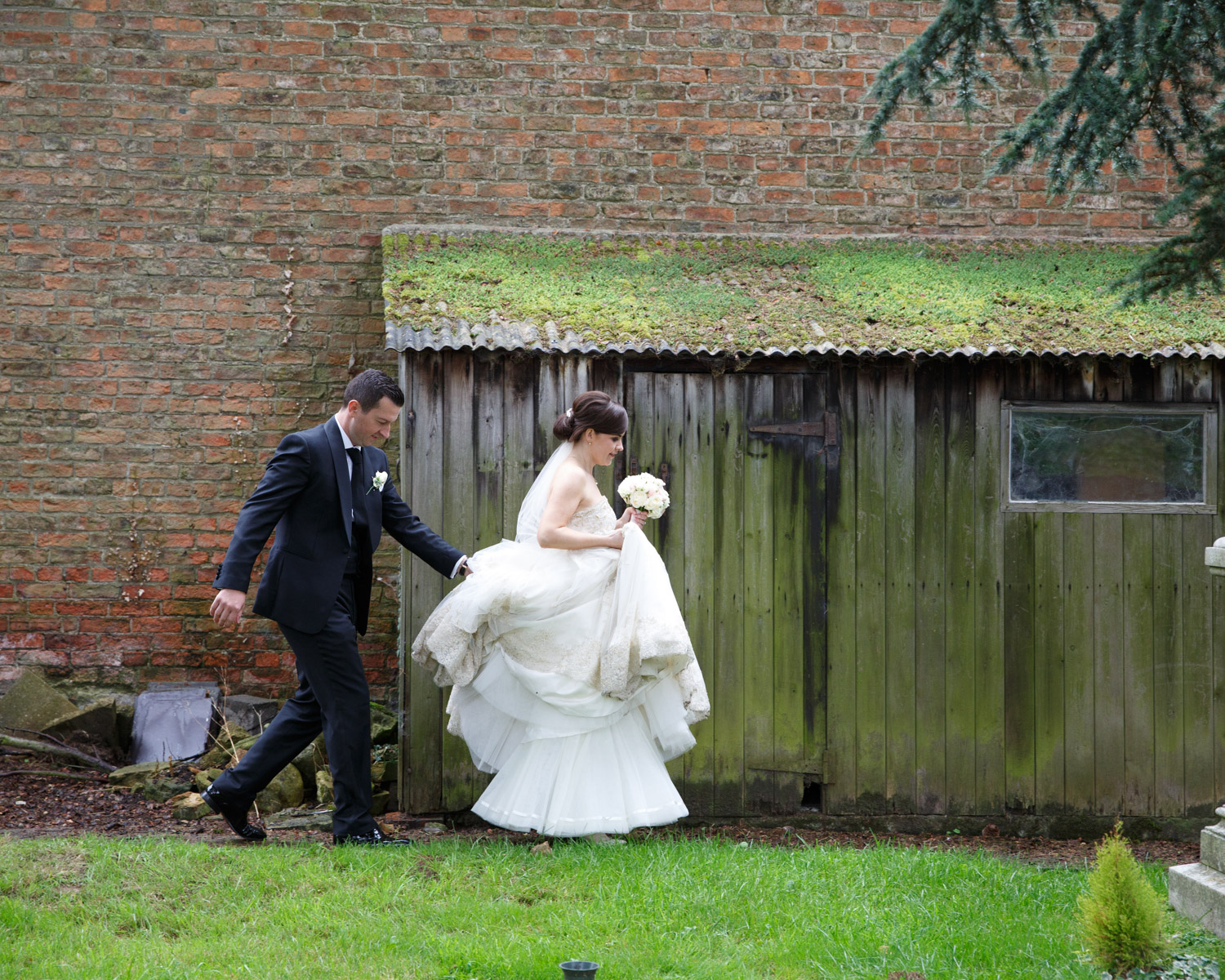 Bride and groom walking a damp woodland path in York, smiles bright through the rain.