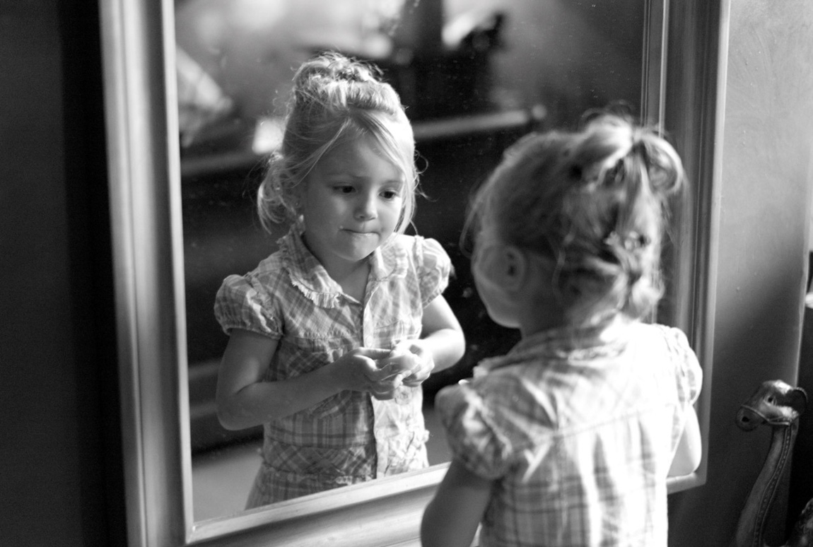 The bride's young daughter doing her make up at the mirror - candid cute moments captured during preparation.