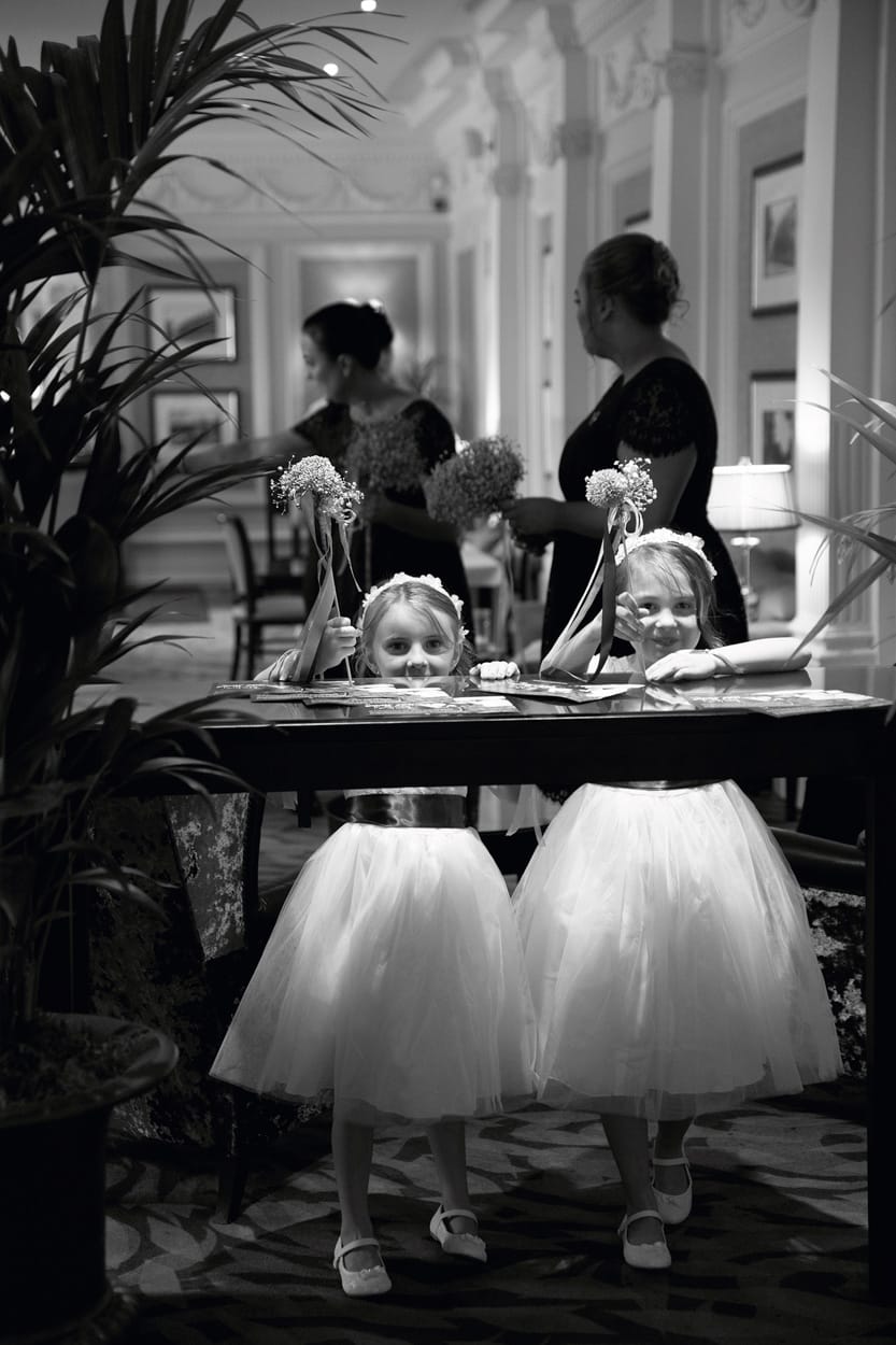 Two young bridesmaids share laughter in soft window light, captured in timeless monochrome. A Candid Leeds wedding photographer at Woodhall Hotel