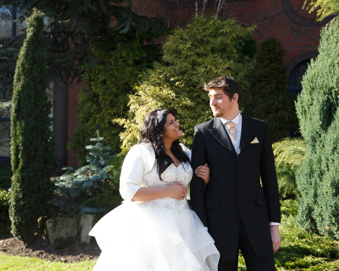 Zehra smiles radiantly beside Richard in the March sunshine as they pause for a wedding portrait at Crowne Plaza Leeds